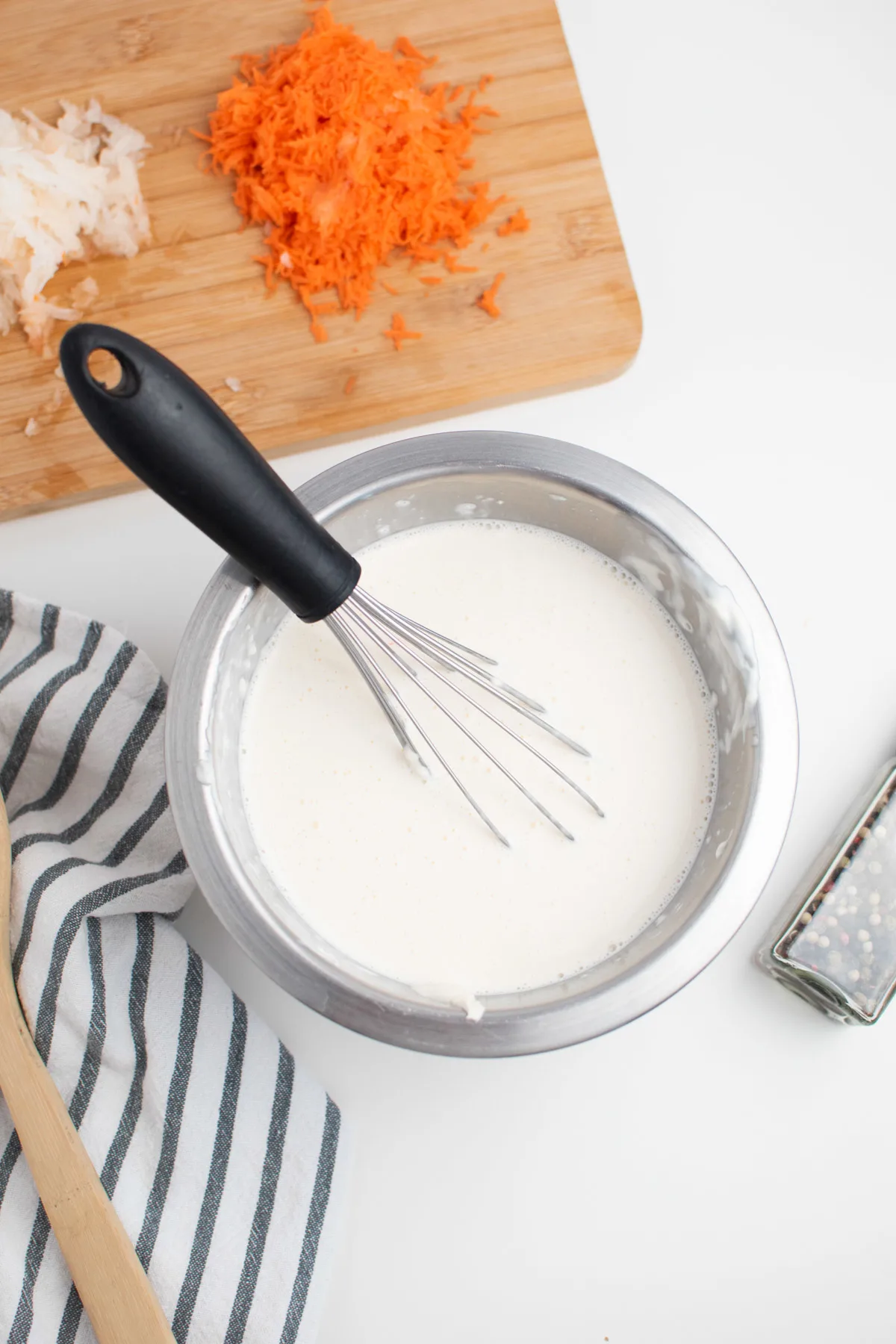 Creamy mayo dressing mixture in small bowl with whisk next to cutting board.