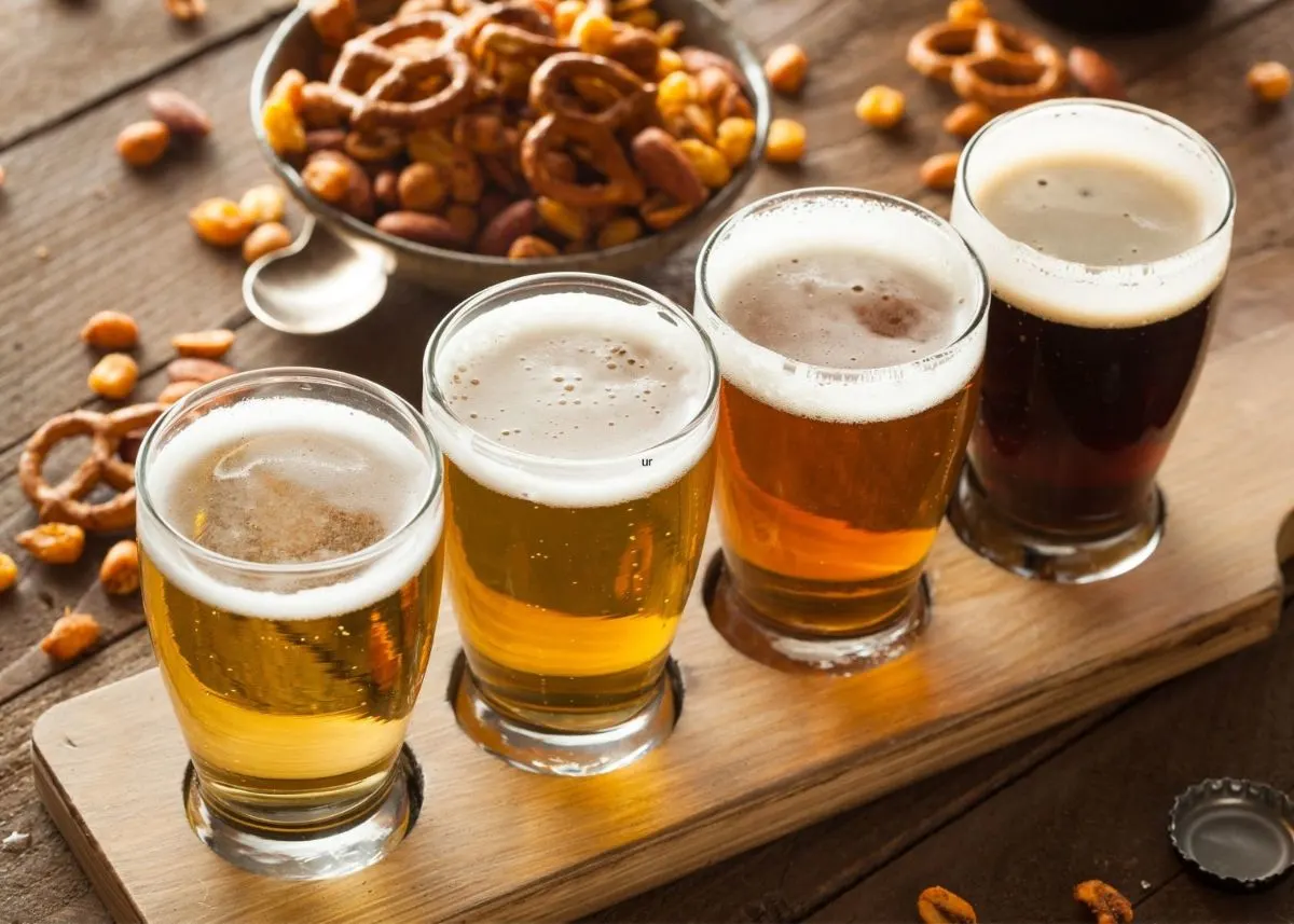 Various beers in clear glass cups with peanuts and pretzels scattered around.