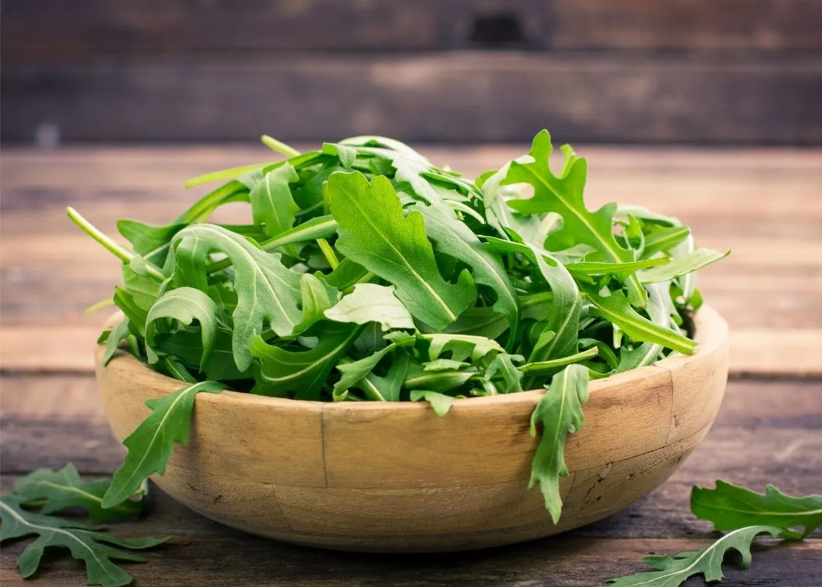 A large pile of arugula leaves heaped in a rustic wooden bowl.