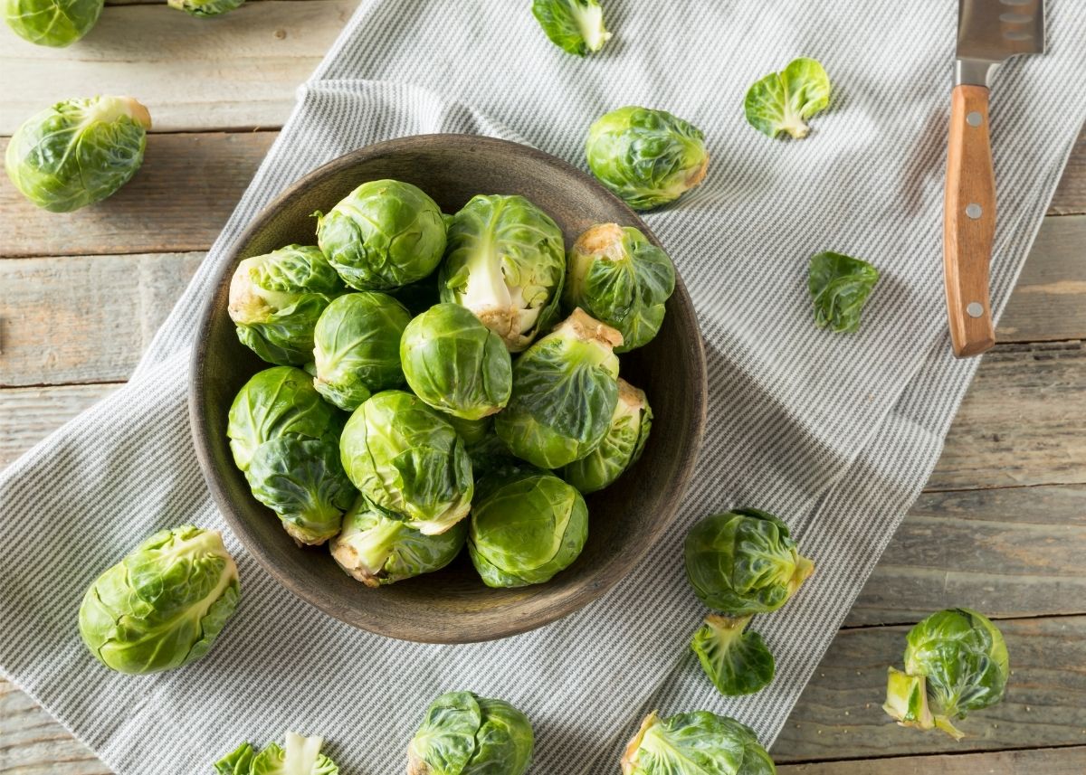 Large wooden bowl filled with brussels sprouts on a light colored kitchen towel.