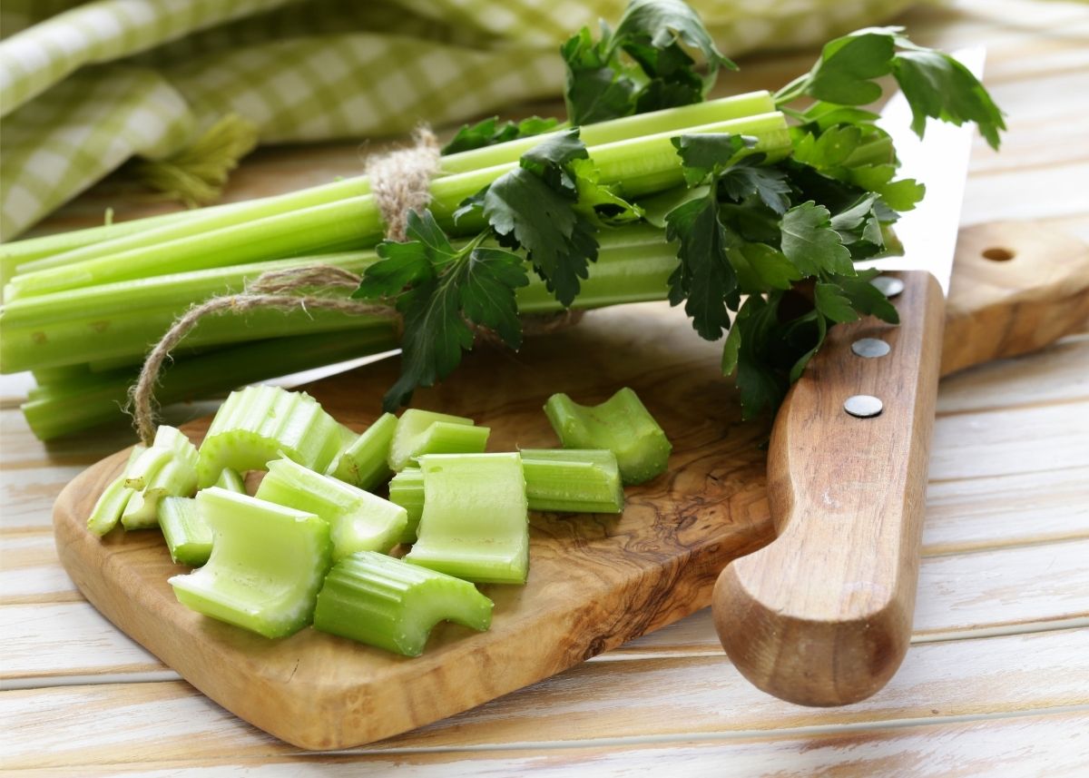 Bundle of celery stalks wrapped in twine next to cut celery on wooden cutting board.