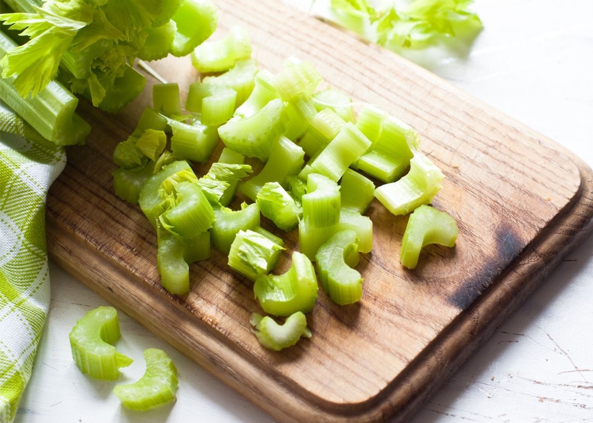 A large pile of chopped celery on a rustic wooden cutting board.