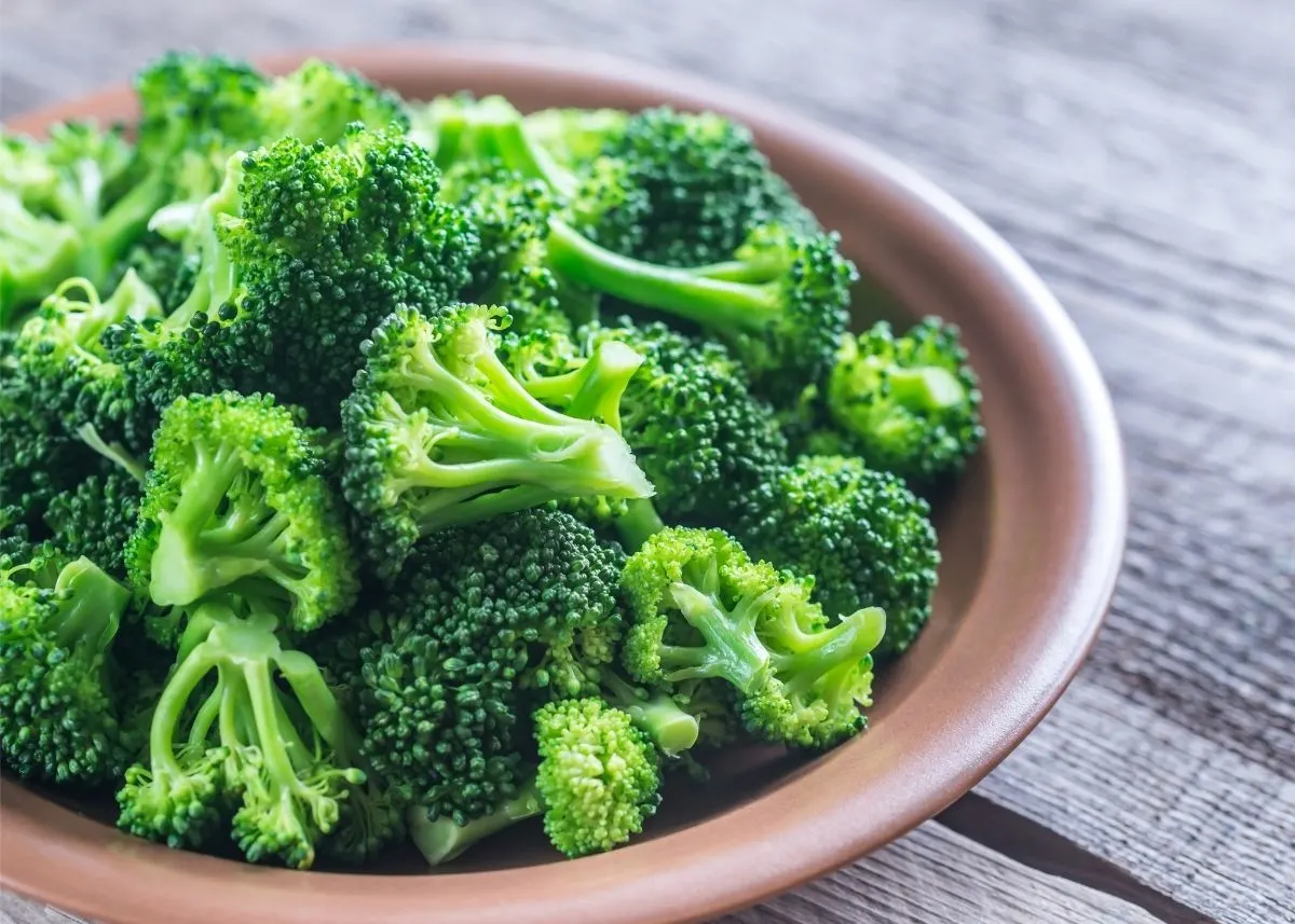 Large brown bowl of bright green cut broccoli on a rustic wooden table.