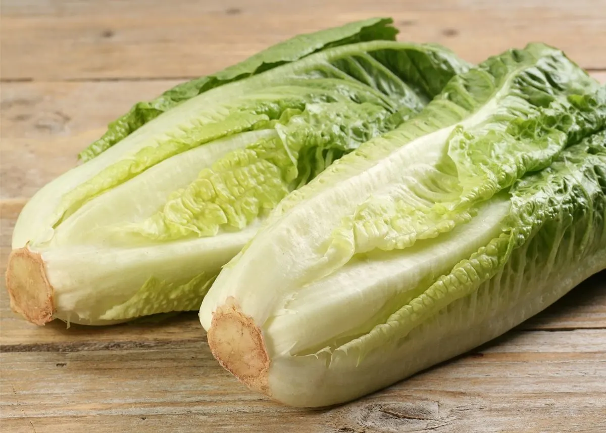 Two hearts of romaine lettuces sitting next to each other on wooden table.