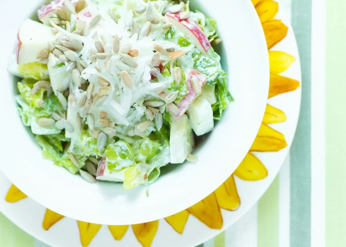 Sunflower seeds garnish a green salad with apples and creamy white dressing.