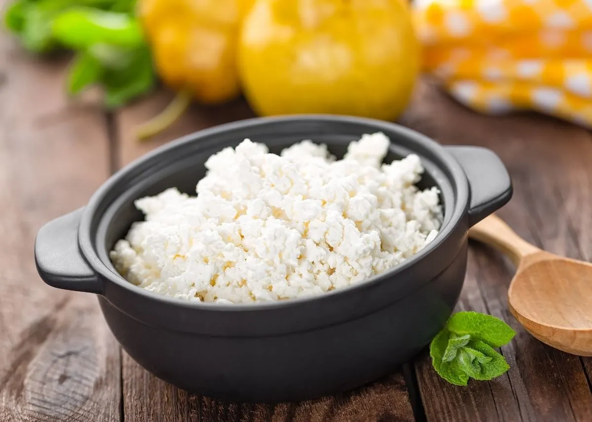 Cottage cheese in a cast iron crock surrounded by yellow and green vegetables.