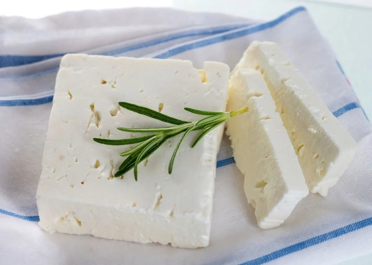 Two large slices of feta cheese garnished with rosemary sprig on blue and white striped kitchen towel.