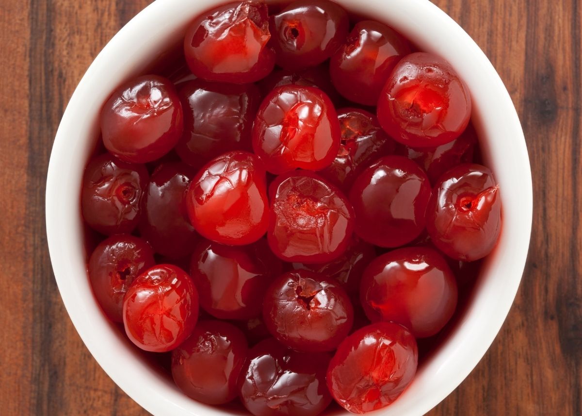 A white bowl filled with red maraschino cherries on a wooden table.