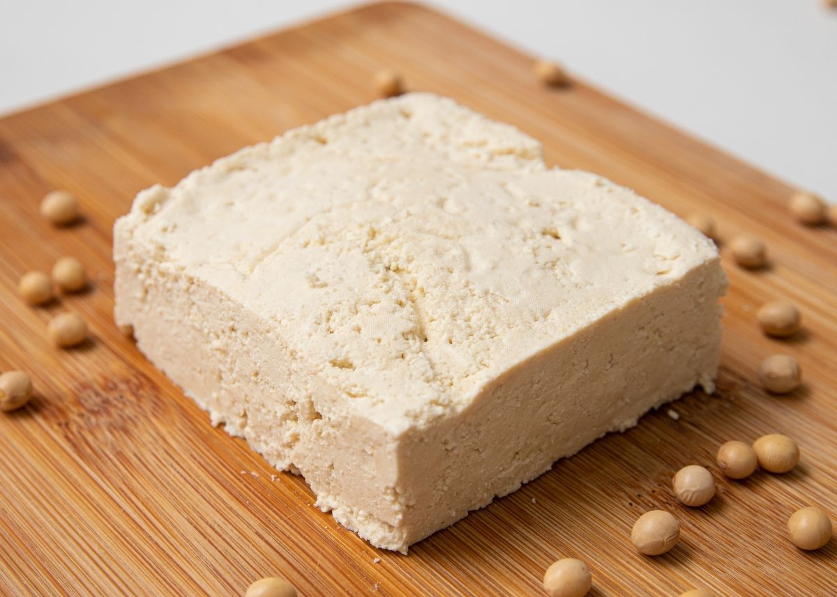 Cotija cheese made from tofu on a wooden cutting board next to soy beans.