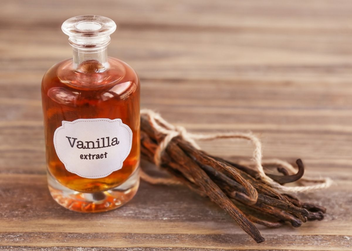 Labeled jar of vanilla extract on a table next to a bundle of vanilla beans.
