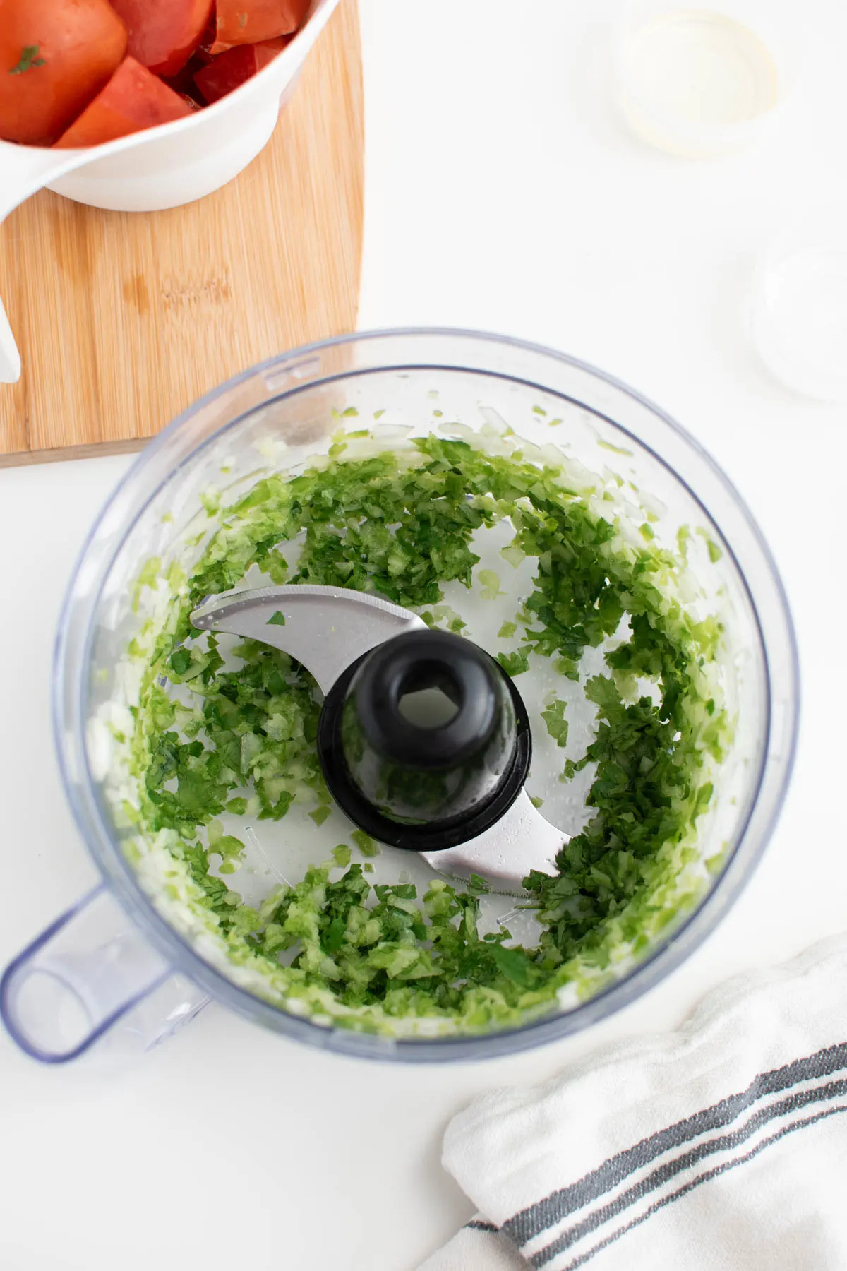 Chopped cilantro, onion, and jalapeno in food processor surrounded by other salsa ingredients.