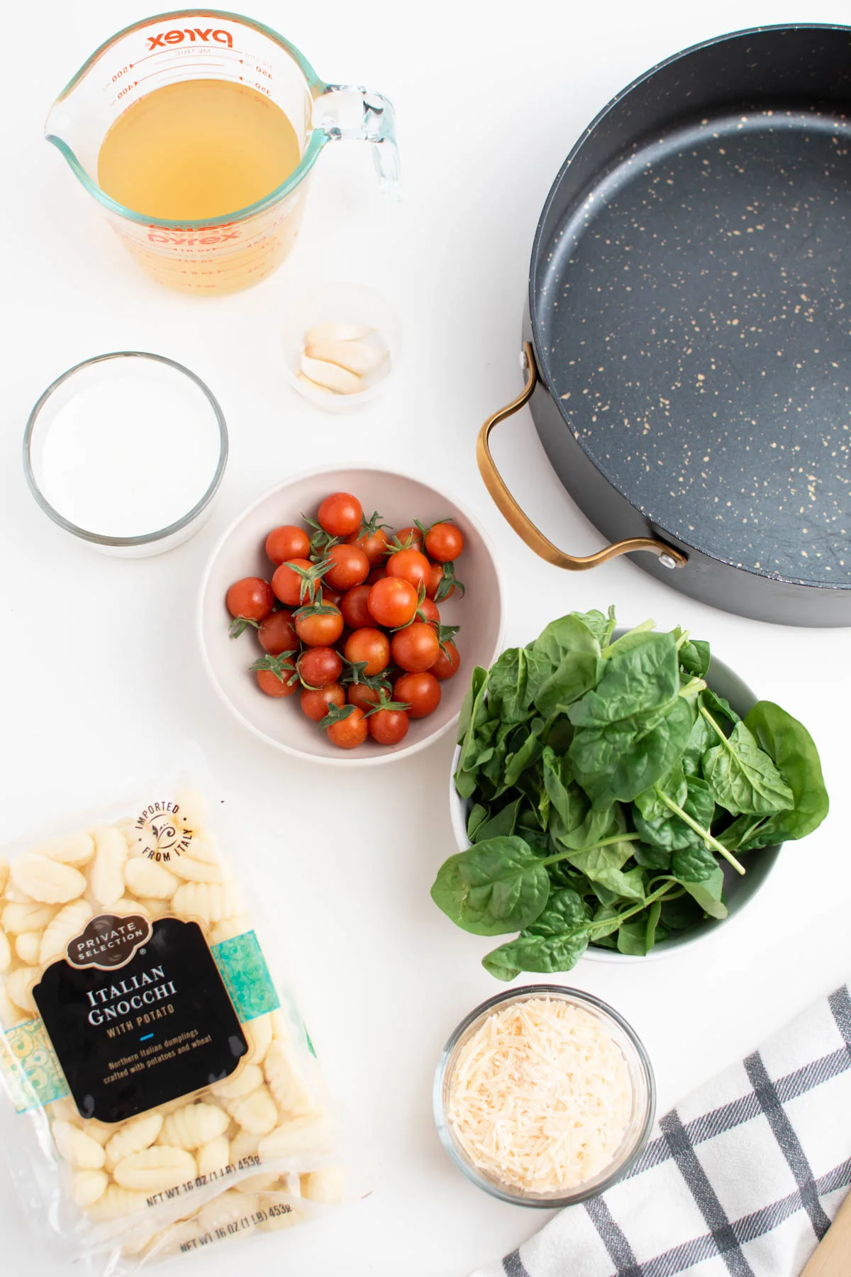 Creamy gnocchi ingredients including tomatoes, spinach, cheese, and cream on white table.