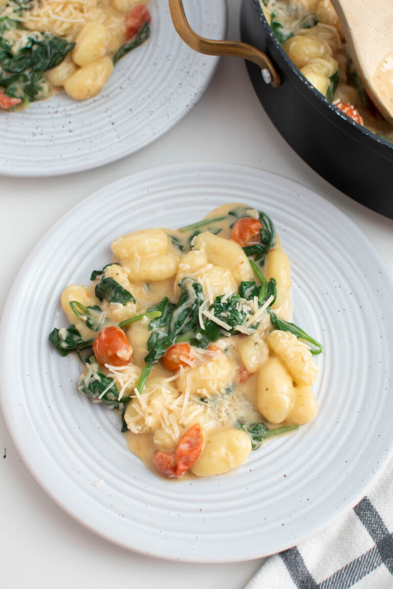 White plate with gnocchi, tomatoes, and spinach in cream sauce.