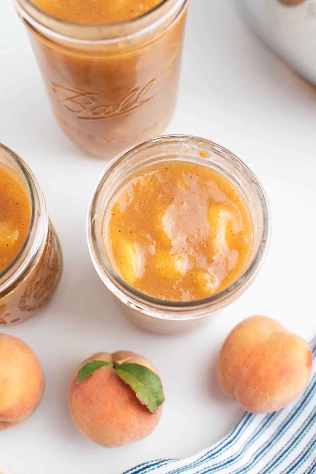 Close up of glass jar filled with peach pie filling surrounded by fresh peaches.