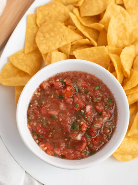 Fresh salsa with tomatoes and cilantro in white bowl surrounded by tortilla chips.