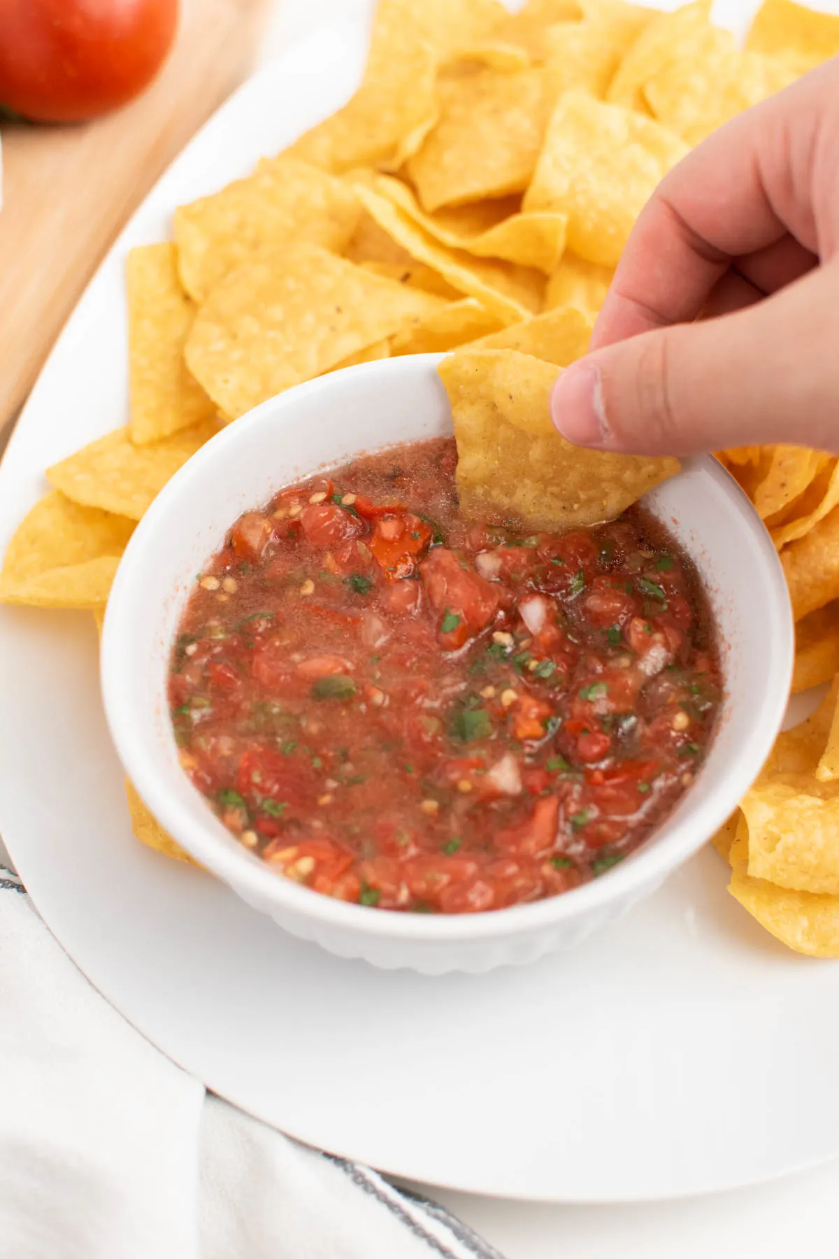 Man dips tortilla chip into garden salsa with tomatoes and cilantro.