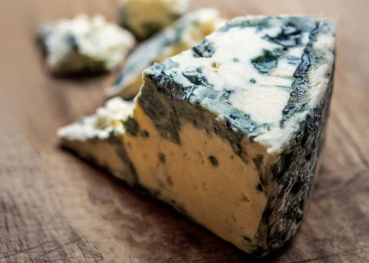 Large wedge of gorgonzola blue cheese with crumbles on a rustic wooden table.