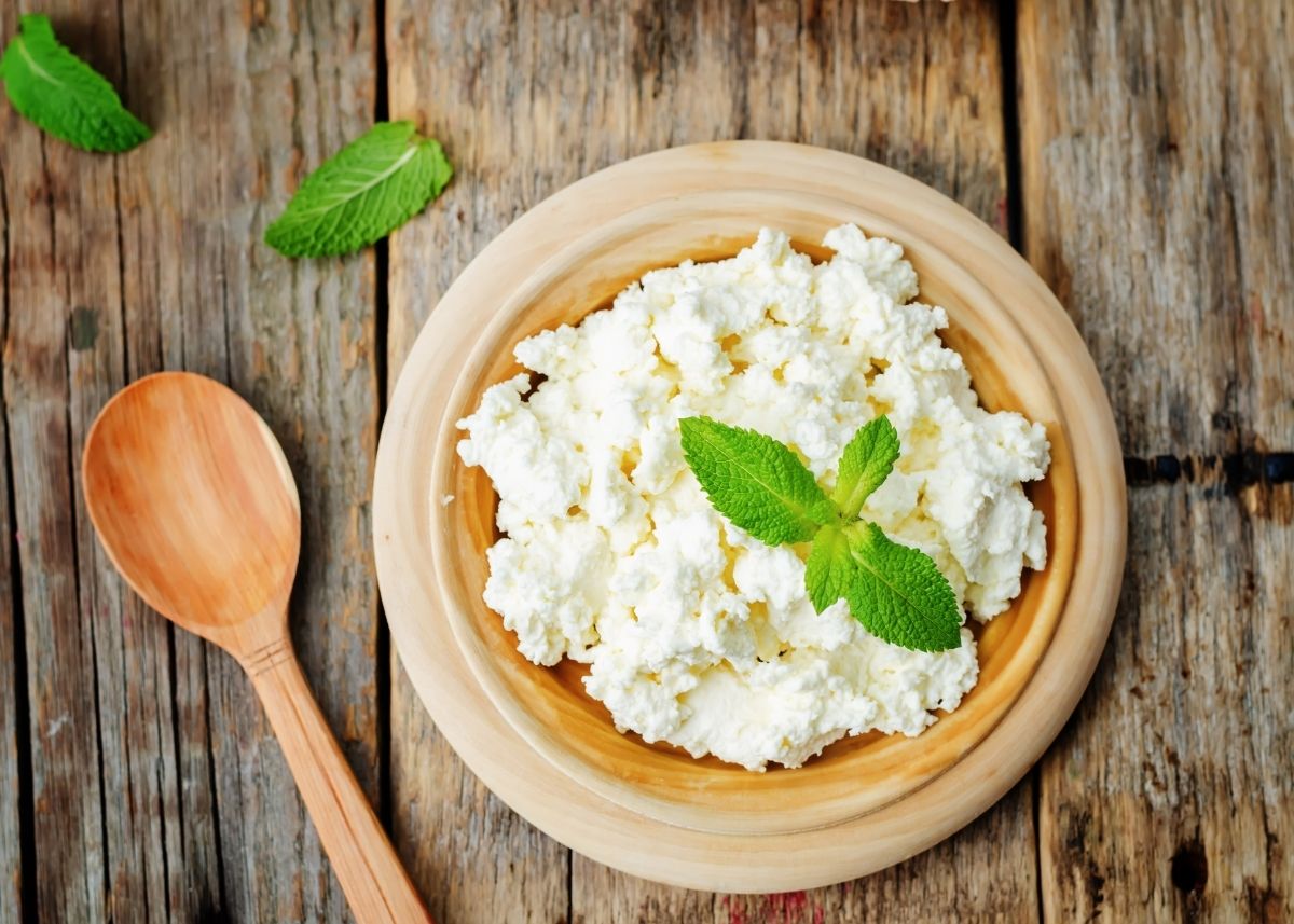 Shallow wooden bowl filled with ricotta cheese with green garnish and wooden spoon.
