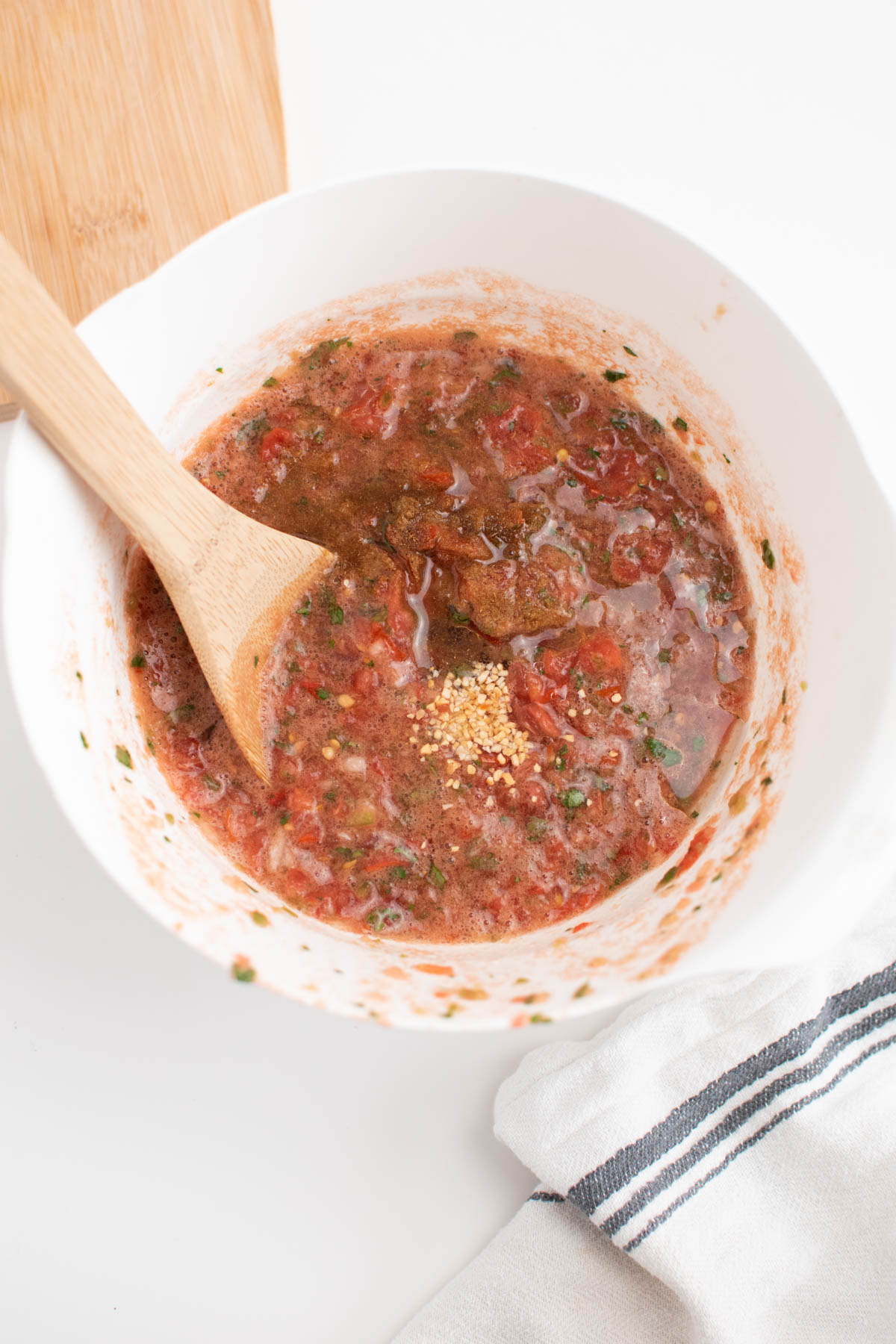 Salsa in mixing bowl with various spices and wooden spoon.