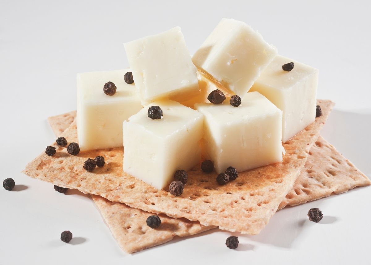 Several cubes of sharp white cheddar cheese and capers on a stack of crackers.