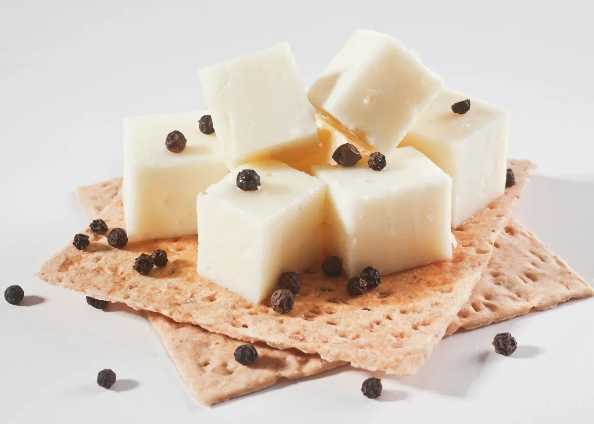 Several cubes of sharp white cheddar cheese and capers on a stack of crackers.