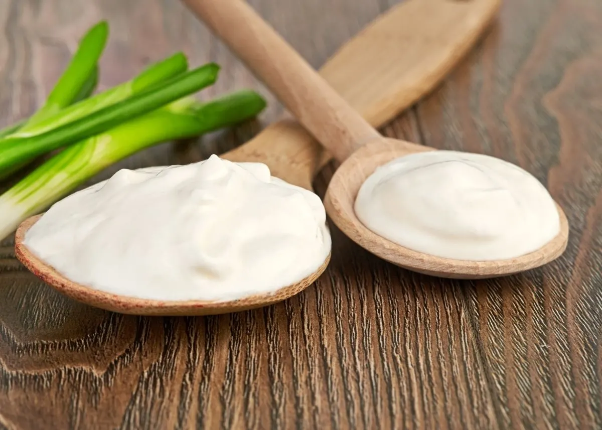 Sour cream on two large wooden spoons next to green onion sprigs.
