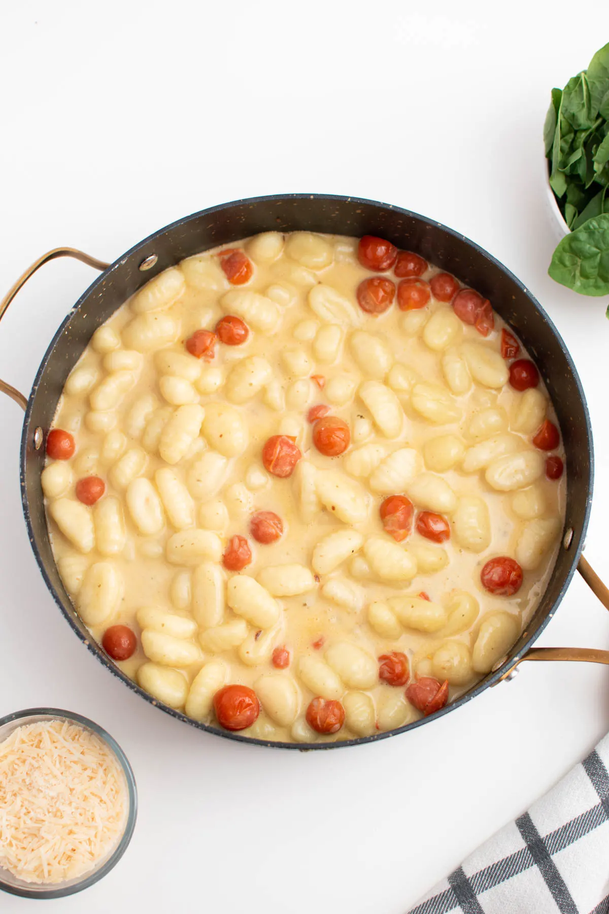 Tomatoes, gnocchi, and creamy sauce in large skillet surrounded by other ingredients.