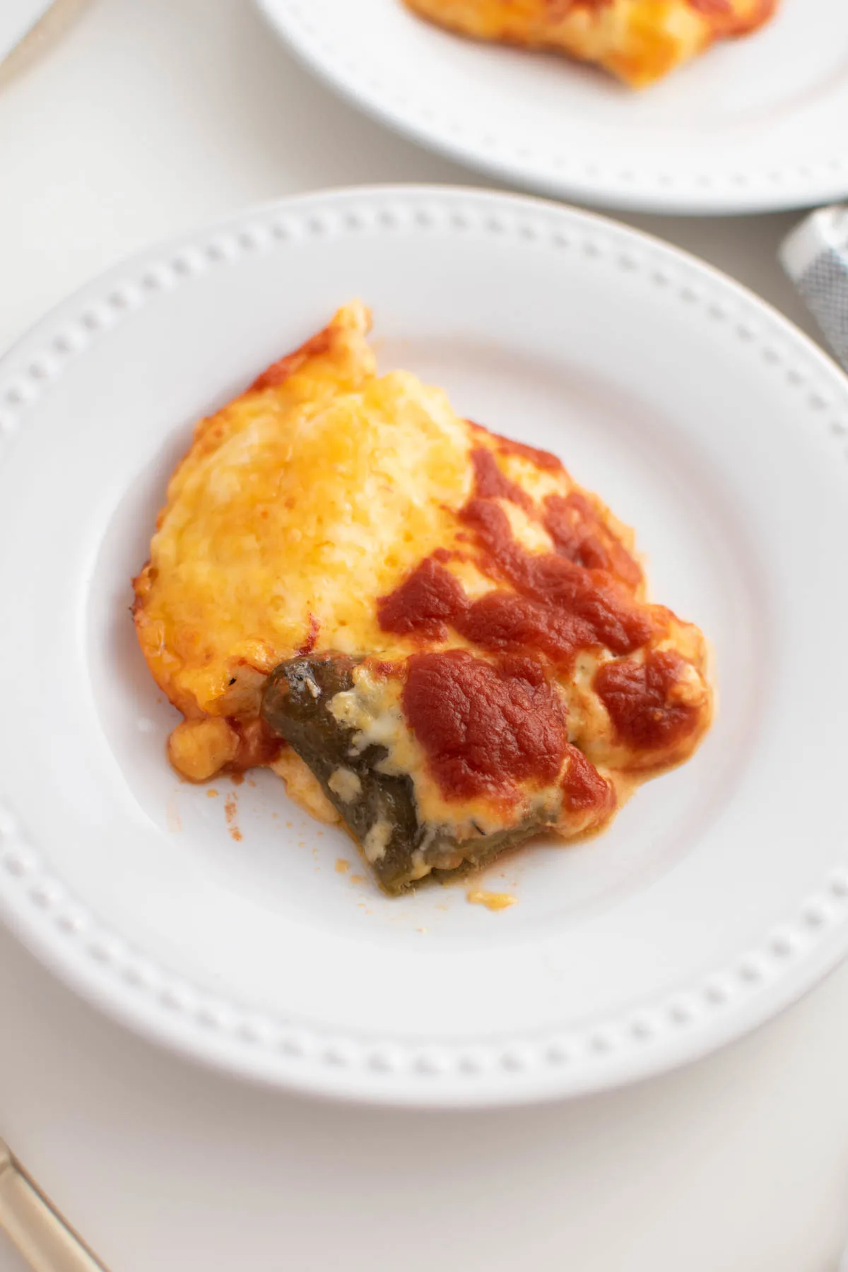 Slice of cheesy chile relleno casserole on white plate sitting on white table.