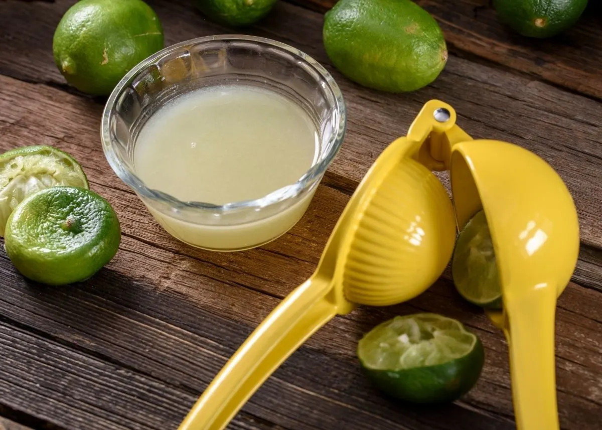 Kitchen tool to squeeze citrus fruits next to bowl of lime juice and fresh limes.