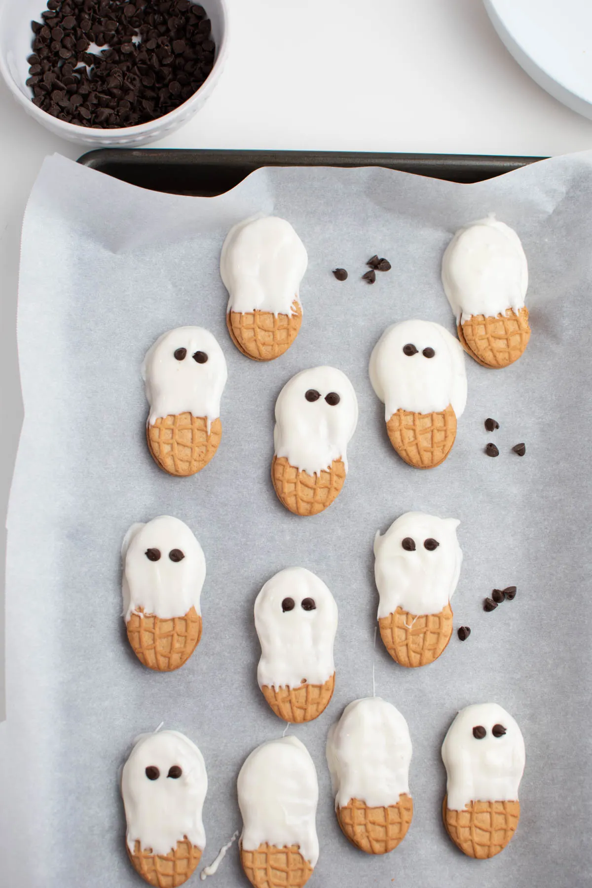 White chocolate dipped cookies on parchment paper with mini chocolate chips for eyes.