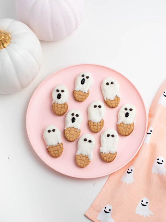 Nutter Butter ghost cookies on pink plate surrounded by ghost towel and painted pumpkins.