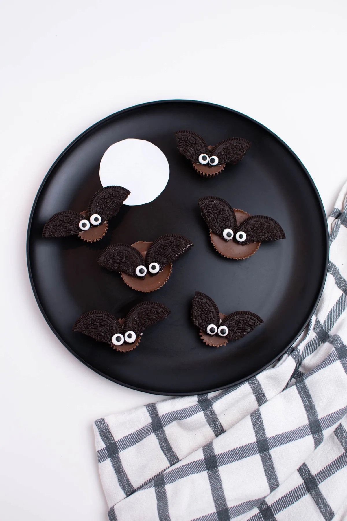 Black plate with a white circle and several Oreo Halloween treats all on white table.