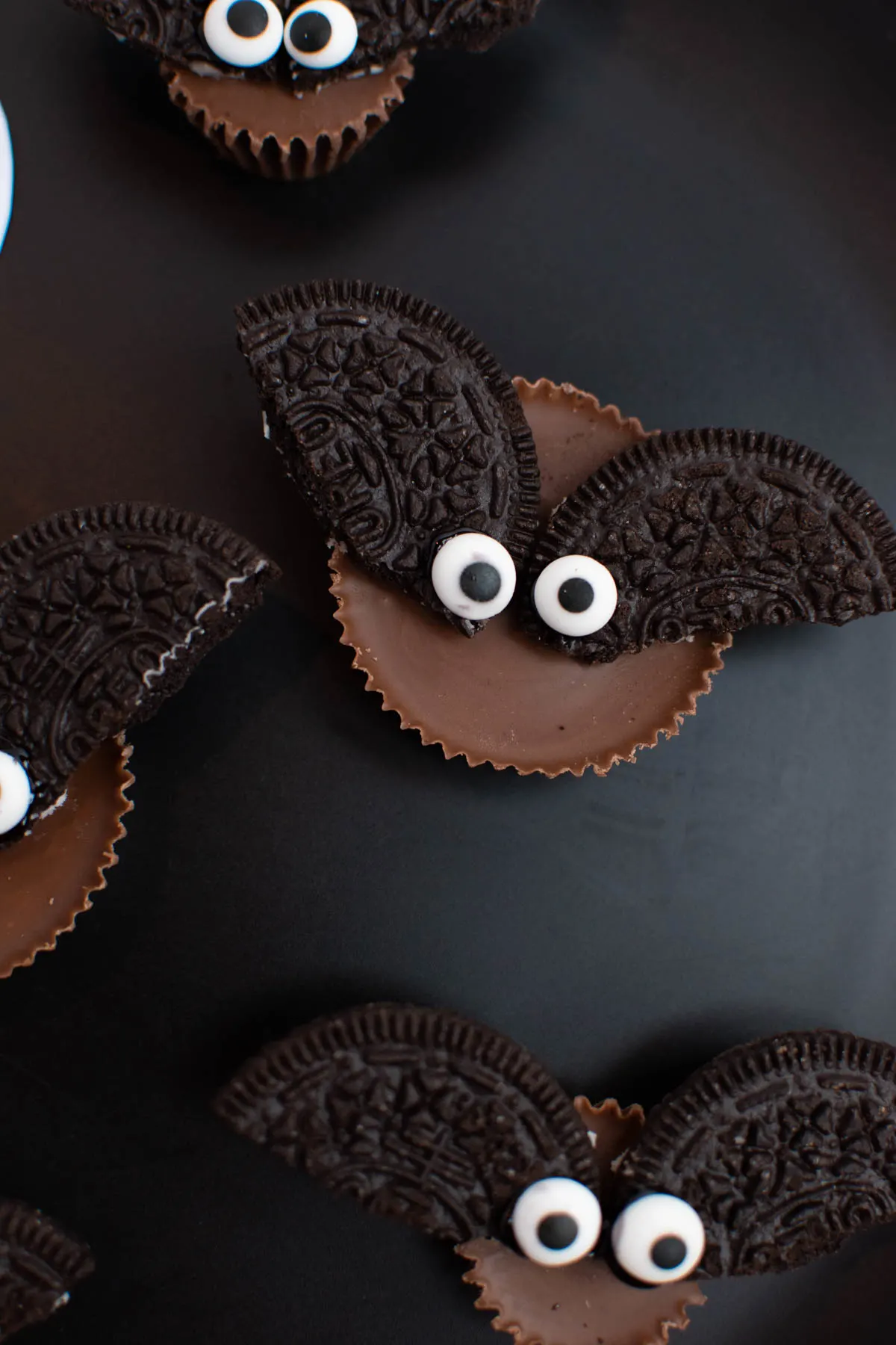 Close up of Reese's Oreo bats with edible eyeballs on black plate.