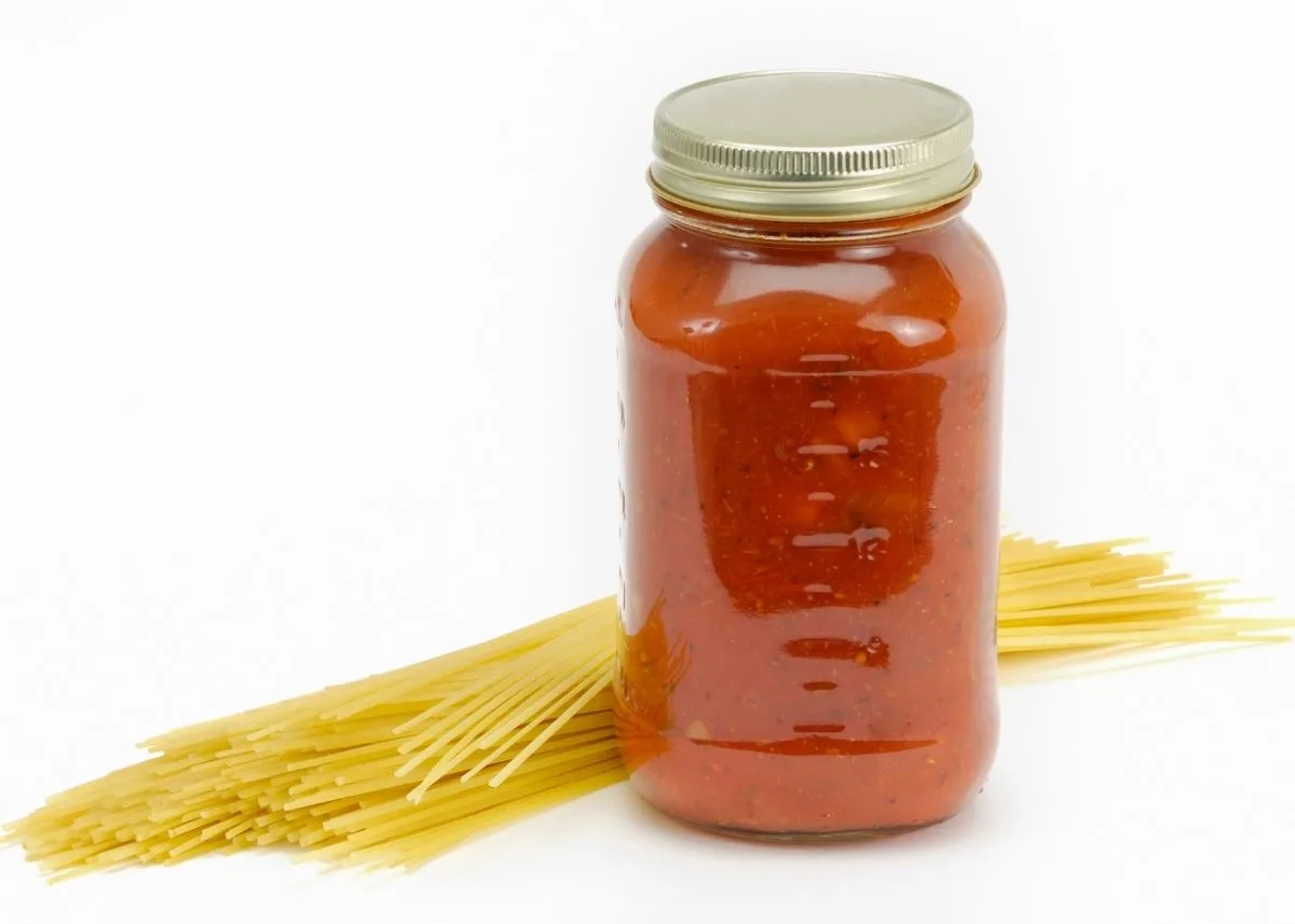 Unopened jar of spaghetti sauce next to pile of uncooked spaghetti noodles.
