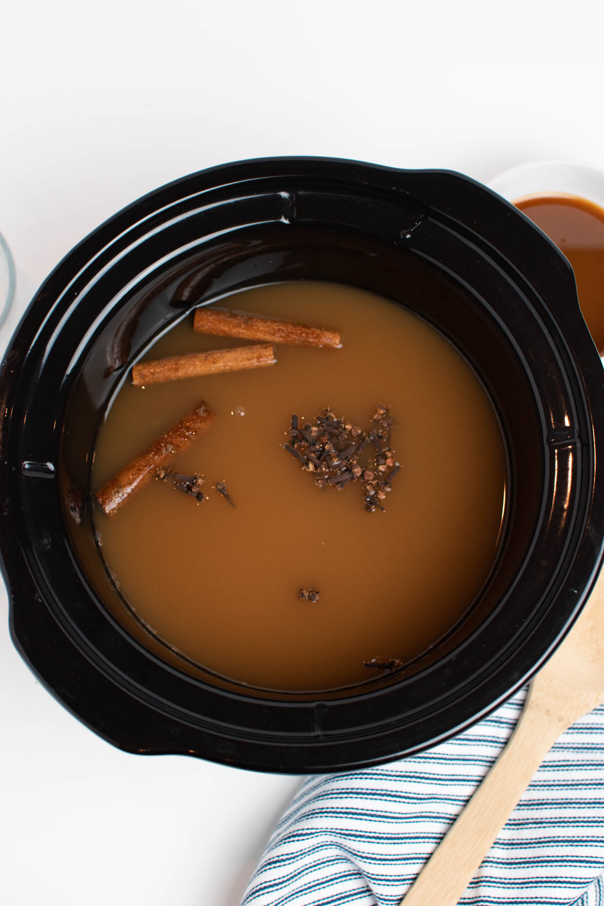 Whole sticks of cinnamon, cloves, and apple cider in black slow cooker insert.