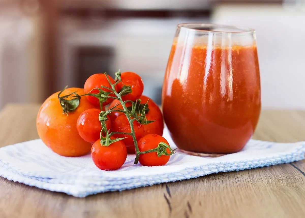 Glass of tomato juice next to whole tomatoes on the vine in kitchen.
