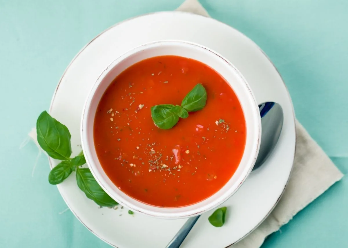 Tomato basil soup in a white bowl on a white saucer with metal spoon.