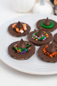 Close up of witch hat cookies with Halloween sprinkle decorations on white plate.