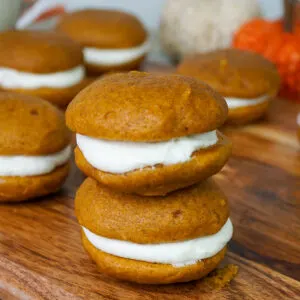 Close up of several pumpkin cookie sandwiches with cream filling on wooden cutting board.
