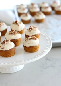Mini pumpkin spice cupcakes with maple cream cheese frosting on a white cake stand.