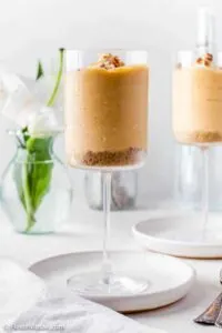 Two glass decorated glasses with long stems filled with no bake pumpkin cheesecake mousse.
