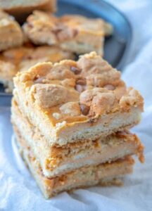 Stack of pumpkin cheesecake bars with chocolate chips on white kitchen towel.