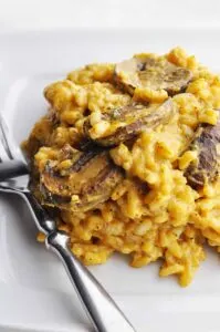 White plate with pumpkin mushroom risotto and silver fork on the side.