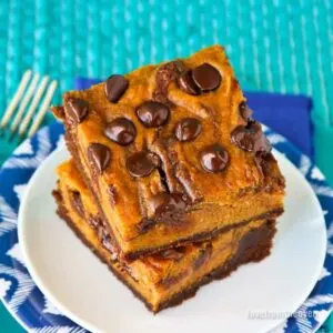 Close up of a stack of pumpkin brownies with melting chocolate chips on top on white plate.