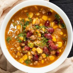 Pumpkin chili with corn, beans and green garnish in large white bowl.