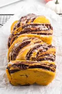 Loaf of pumpkin chocolate babka on parchment paper and wire cooling rack.