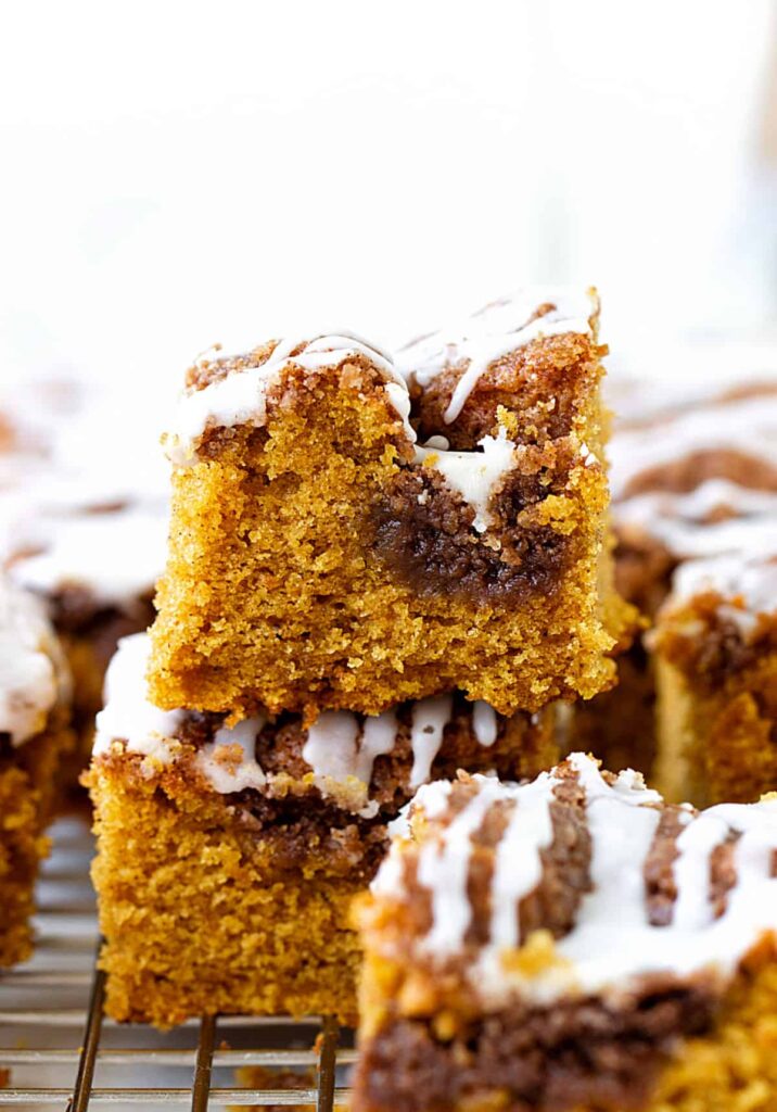 Squares of pumpkin coffee cake with icing stacked on each other.