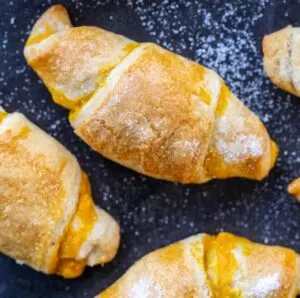 Close up of fluffy pumpkin croissants sprinkled with sugar on a black background.