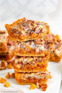 Close up of several stacked pumpkin magic bars with pecans on white surface.
