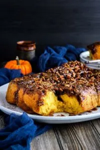 Pumpkin sticky buns topped with chopped nuts on white serving platter next to blue kitchen towel.